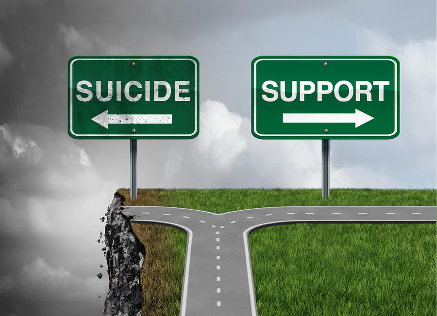 Two road signs with the words suicide over a cliff and the word support with a road