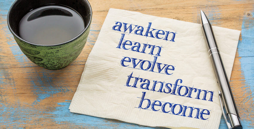 A cup of coffee with the words awaken, learn, evolve, transform, & become on a napkin